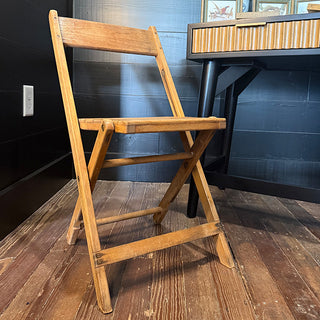 Vintage wooden folding chair with slatted seat and backrest displayed beside a modern desk on rustic wooden flooring
