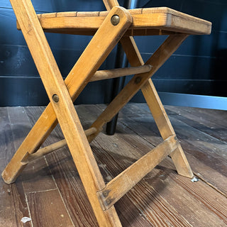 Side view of an antique wooden folding chair highlighting its cross-braced legs and solid craftsmanship