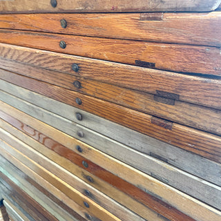 Detailed view of stacked wooden folding chairs in mixed wood finishes, showcasing natural patina and rivet joint
