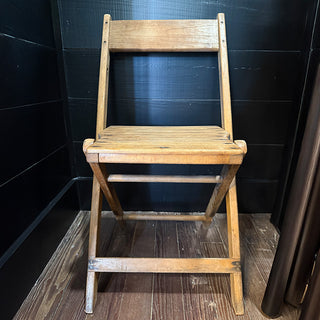 Front view of a classic wooden folding chair with slatted seat and backrest placed against a black wall