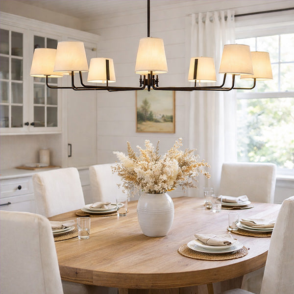 Modern 8-light black iron chandelier with white fabric shades over dining table in bright white kitchen