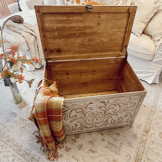 Open carved wood storage chest with throw blanket