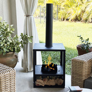 Outdoor chiminea fireplace with burning fire surrounded by wicker patio furniture and lush greenery.