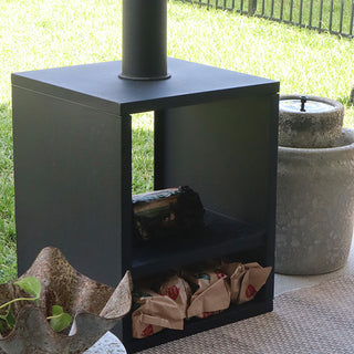 Close-up of modern black chiminea on a patio showing wood-storage compartment and outdoor decor