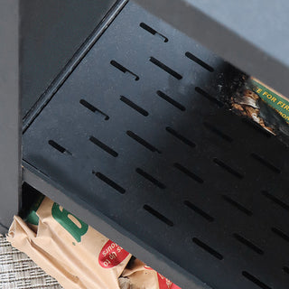 Detailed view of the chiminea’s slotted metal grate and wood-storage shelf on a backyard patio.