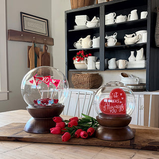 Spherical glass cloche set with walnut wood pedestal bases displayed on farmhouse dining table with seasonal decorations