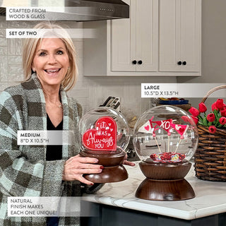 Set of two decorative globe-shaped glass domes on rich wood bases showcasing Valentine's Day décor