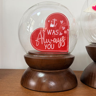 Close-up of medium spherical glass cloche with decorative heart display on warm wood pedestal base