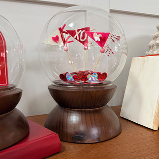 Large glass globe cloche with Valentine pennant flags and heart confetti on walnut wood stand