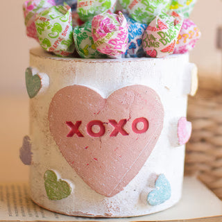 Close up clay XOXO conversation heart container filled with Dum Dum lollipops showing pink heart design and dimensional pastel hearts Valentine candy display