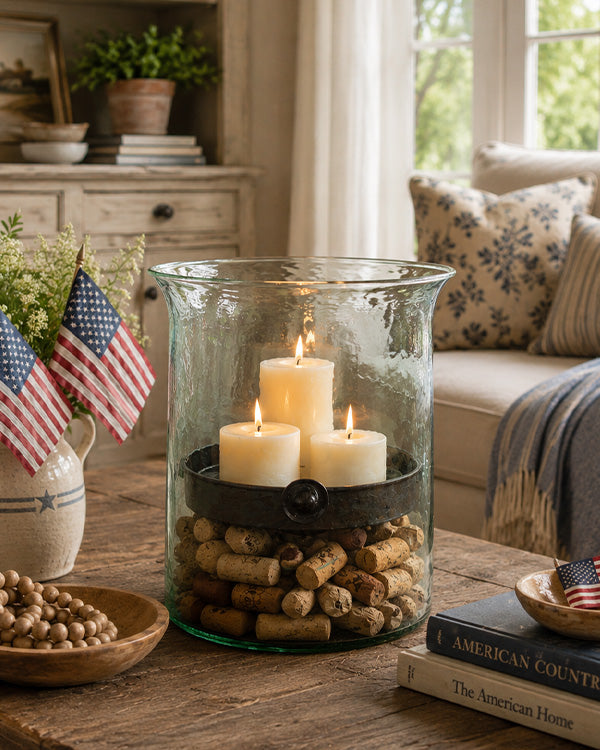 Decorative setup with candles in a glass container, American flags, and books on a wooden table.