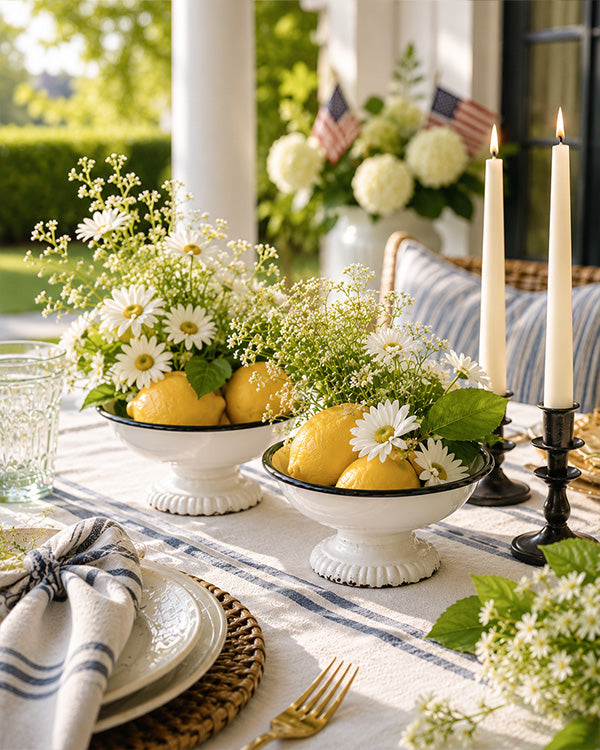 Outdoor table setting with lemons, flowers, and candles on a striped tablecloth.
