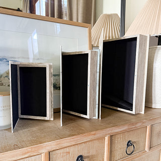 Three faux book storage boxes opened to reveal black velvet-lined interior compartments for hidden storage.