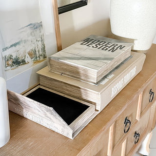 Decorative faux book storage boxes displayed on a wood console table, with one book open to reveal hidden velvet-lined storage