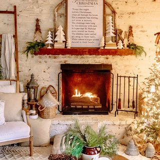Cozy farmhouse living room with lit brick fireplace, Christmas mantel decor, and black iron fireplace tool set arranged neatly beside the hearth.