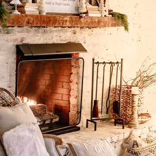 Rustic brick fireplace with glowing fire, wooden mantel decor, and iron fireplace tool set placed on stone hearth in a warm holiday setting.