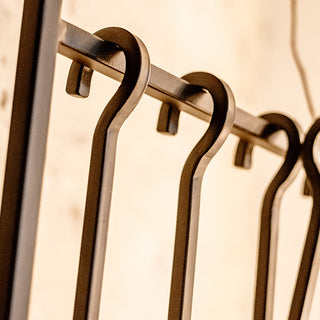 Close-up of iron hooks holding fireplace tools, showing detailed craftsmanship and matte black finish for home decor and hearth organization.