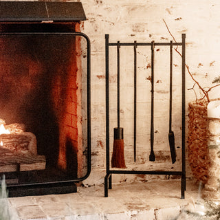 Black iron fireplace tool set arranged beside active brick fireplace, styled with cozy holiday home decor elements on the hearth.