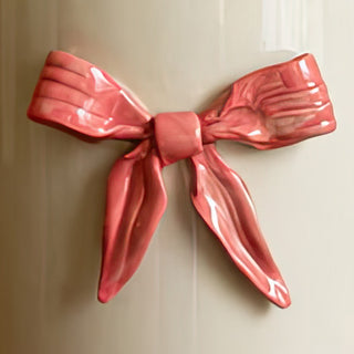 Close-up detail shot of sculptural glossy pink ceramic bow decoration on cream white holiday planter showing hand-painted craftsmanship and three-dimensional design