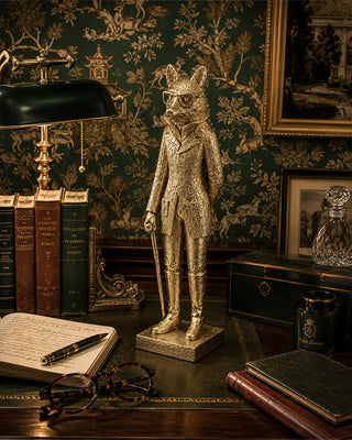 Gold fox statue on a desk with books and a lamp in an ornate room.