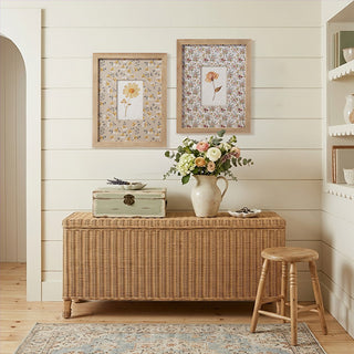 Pressed flower framed wall art set displayed on white shiplap wall above wicker storage trunk