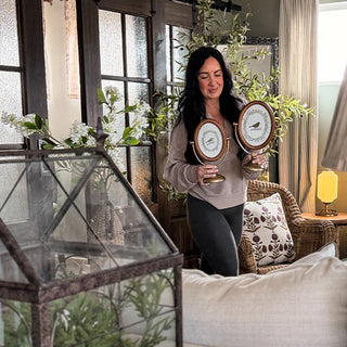 Woman holding two decorative clocks in a home setting with plants and furniture. Oval Photo Frame, Set of 2 | Antique Brass Stand Vintage Tabletop Picture Frame
