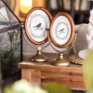 Two oval photo frames with bird illustrations on a wooden surface. Oval Photo Frame, Set of 2 | Antique Brass Stand Vintage Tabletop Picture Frame