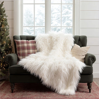 Luxurious white faux fur throw blanket draped over green velvet chair in cozy Christmas farmhouse living room with plaid pillows