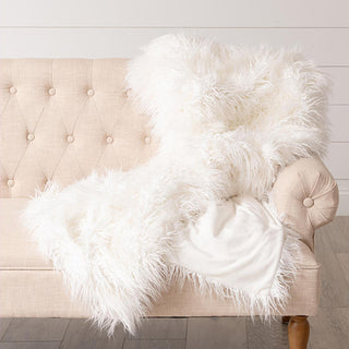 Cream white faux fur throw blanket displayed on elegant tufted beige chair showing versatile neutral color and luxurious drape