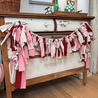 Full view of 60-inch fabric ribbon tassel garland draped on distressed white wood furniture Valentine's decor