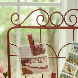 Close-up of vintage-inspired red metal gate stand with clothespin clips holding nostalgic photos near window