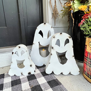 Trio of white metal ghost Halloween candle holders with rustic finish displayed on black-and-white plaid doormat