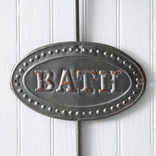 Close-up of distressed metal "BATH" plaque on rustic farmhouse towel hook
