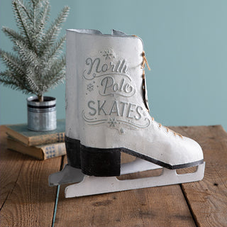 Single white metal North Pole Skates decorative ice skate with jute laces, displayed on wooden table with small pine tree in background