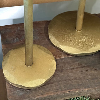 Close-up of the circular textured gold bases of forged-iron taper candle holders on a wooden surface.