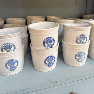 Stack of small vintage Belgian stoneware jars with blue Frameries logo on wooden shelf, rustic European kitchen decor
