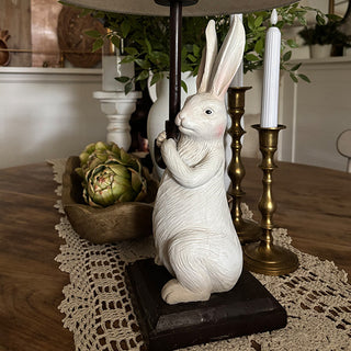 Decorative white rabbit figurine on a table with candles and plants in the background