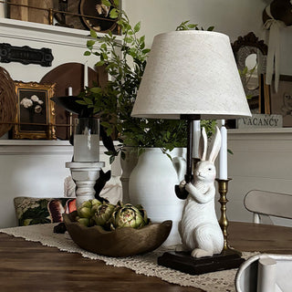 Decorative table setting with a rabbit figurine lamp, plants, and candles.