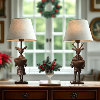 Pair of reindeer-themed table lamps with beige shades and bronze bases on a holiday-decorated console table