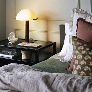 Modern white mushroom table lamp with bronze base on black nightstand in contemporary bedroom