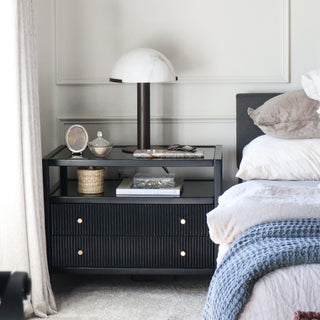 Modern mushroom table lamp with white dome shade on black nightstand beside bed with blue throw