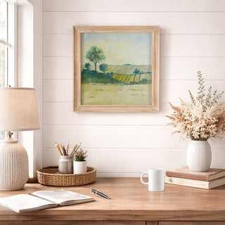 Handcrafted watercolor landscape painting with natural wood frame displayed on white shiplap wall above farmhouse desk with lamp and dried flowers