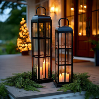 Set of tall black metal and glass lanterns with glowing pillar candles on a decorated front porch, holiday home décor lighting