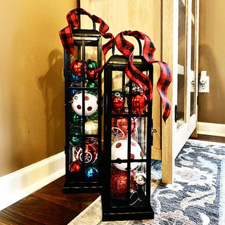 Black glass lanterns filled with colorful Christmas ornaments and red plaid ribbon bows, festive holiday home décor accent