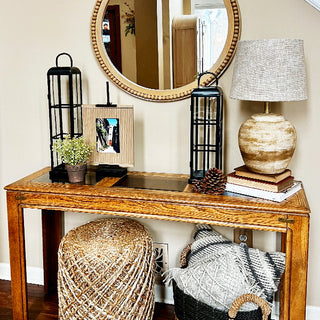 Entryway console table styled with matching black lantern set, round mirror, woven basket, and neutral home décor accents.
