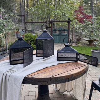 Black iron lanterns with open hinged doors showcased on a wooden patio table, highlighting functional candle-access design.