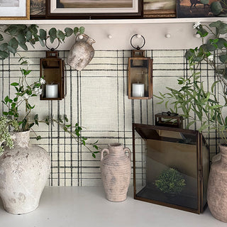 Wall-mounted bronze lanterns with pillar candles styled on a plaid-pattern backdrop alongside rustic vases and greenery for elegant home décor.