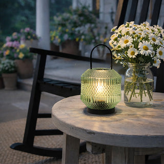 Green tinted glass LED lantern on wooden patio table at dusk
