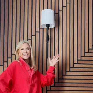 Close-up of black metal arm wall sconce with white drum shade installed on decorative wall panel