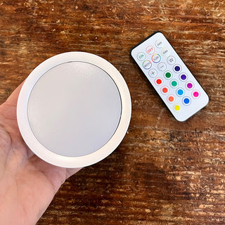 Rechargeable LED bulb puck light with remote control showing RGB color options for wall sconce